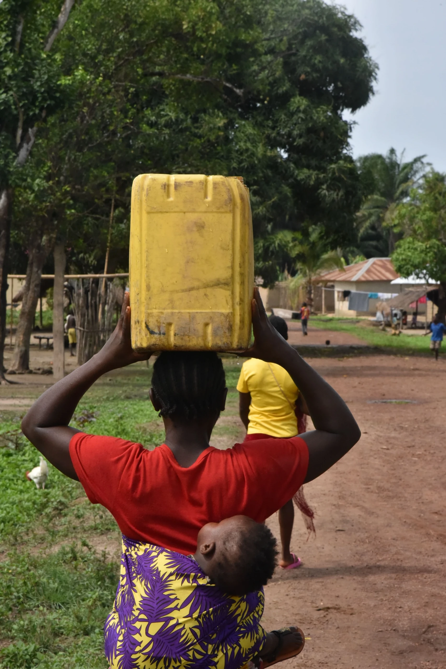 Aminata Bangura cargando un bidón de 20 litros con agua potable sobre su cabeza. Lleva en la espalda a su bebé para ir a su hogar en Masiperr, en el distrito de Tonkolili © Daniel García / MSF