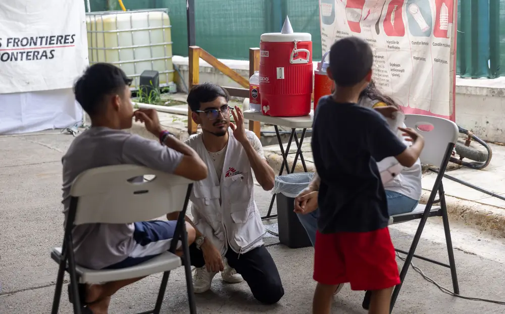 Trabajador de MSF conversa con dos niños en el albergue Pumarejo, en Matamoros, México.