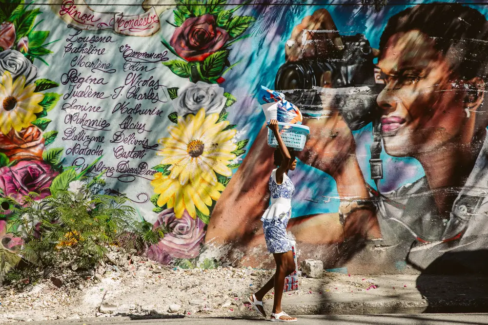 Una mujer caminando frente a un mural realizado en honor a Regina Nicolas, asesinada por su pareja, en Lalue, un barrio residencial de Puerto Príncipe.