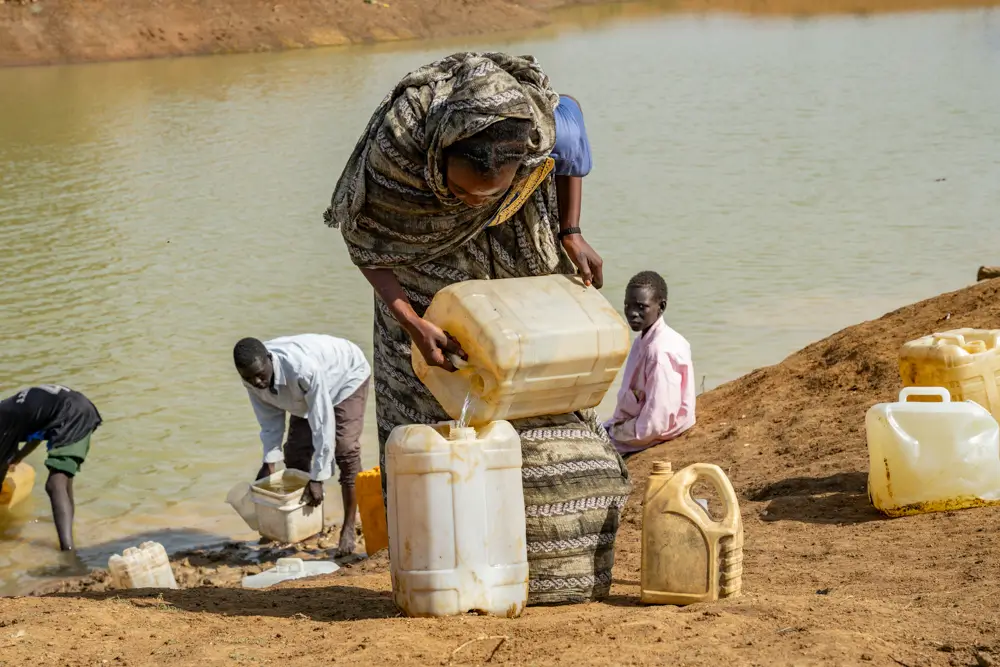 Varios habitantes del asentamiento informal de Atam recogen agua de un estanque con bidones. Los equipos de MSF están trabajando para tratar el agua y garantizar el suministro de agua potable a las personas desplazadas que huyen de la guerra en Sudán.