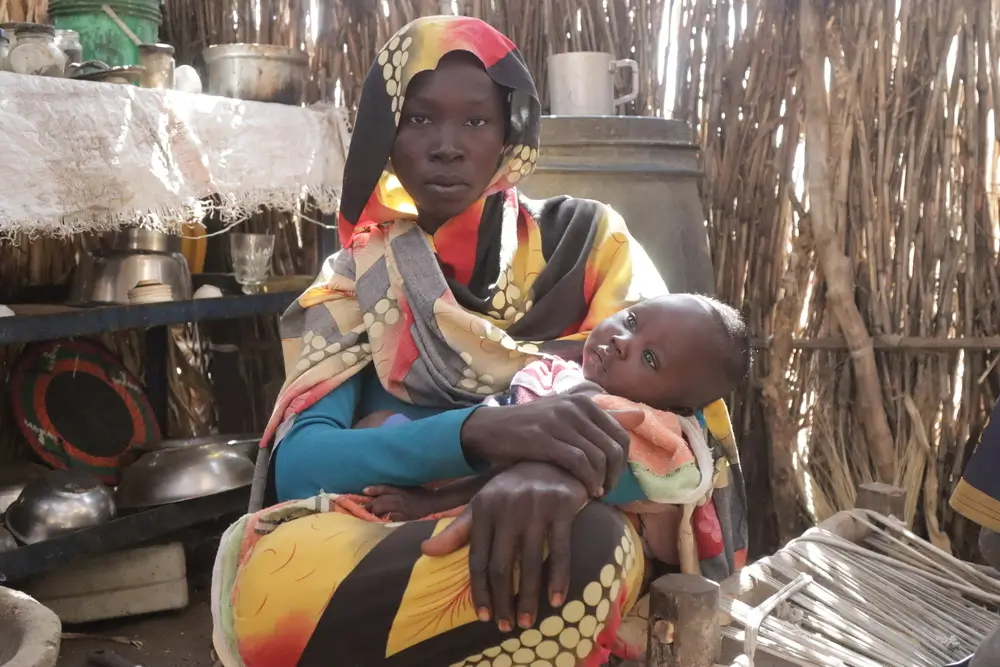 Zahra Abdullah sostiene a su bebé en la cocina de un refugio tras recibir su cesta de comida. Darfur Sur, Sudán, enero de 2025.
