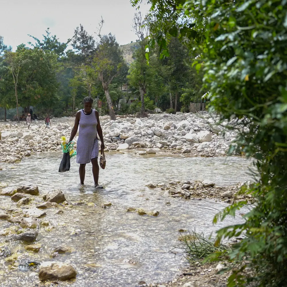 Manita, embarazada de siete meses, cruza el río casi seco de camino a casa tras una cita médica en el Centro de Salud Rendel. Le espera una caminata de dos horas, ya que no hay transporte en la zona debido a las carreteras intransitables.