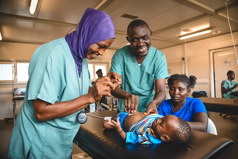 La mentora clínica, Momoh Sao, y la auxiliar de enfermería, Aminata Koroma, examinan a Ogar Boima, de 6 meses, en la sala de urgencias del hospital maternoinfantil de MSF en el distrito de Kenema. Sierra Leona, mayo de 2025.