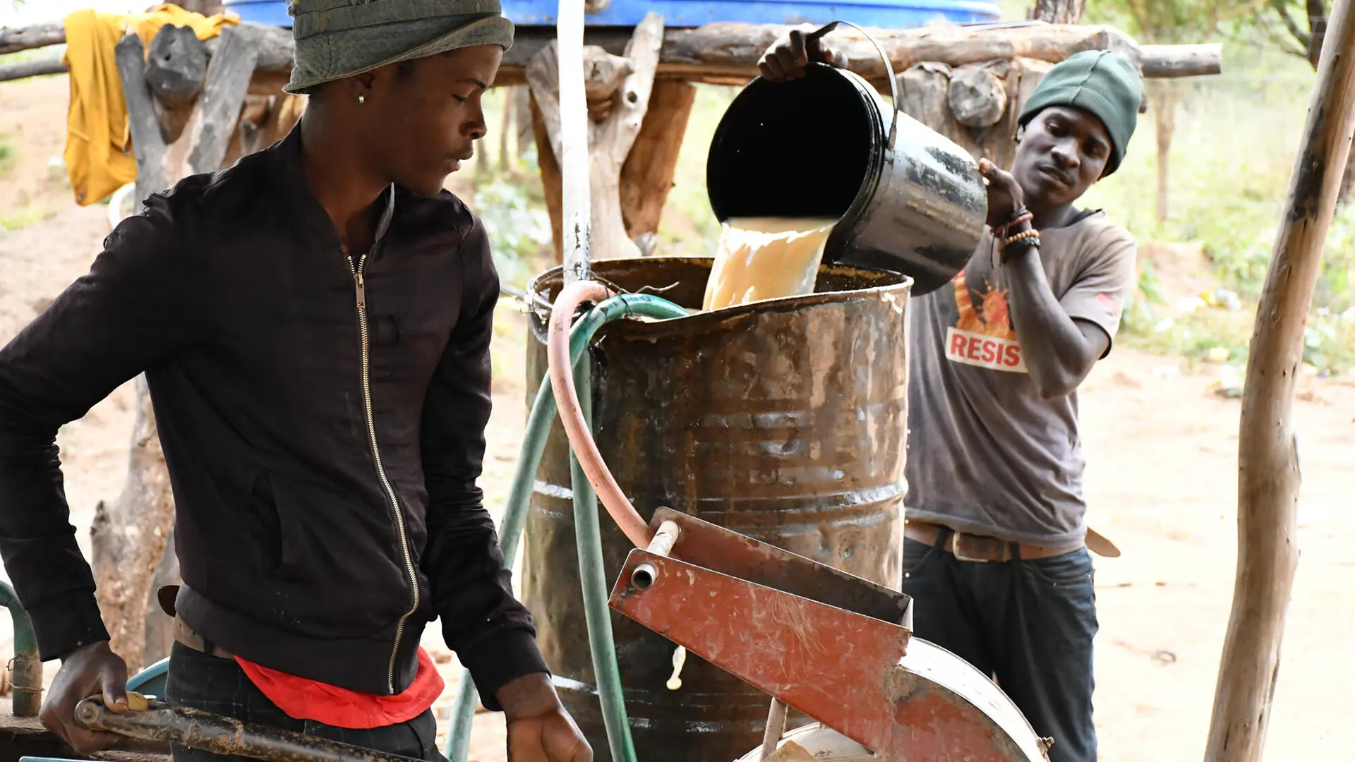 Dos mineros artesanales que trabajan juntos: uno carga mineral en el molino mientras el otro agrega agua para ayudar en el proceso de separación.