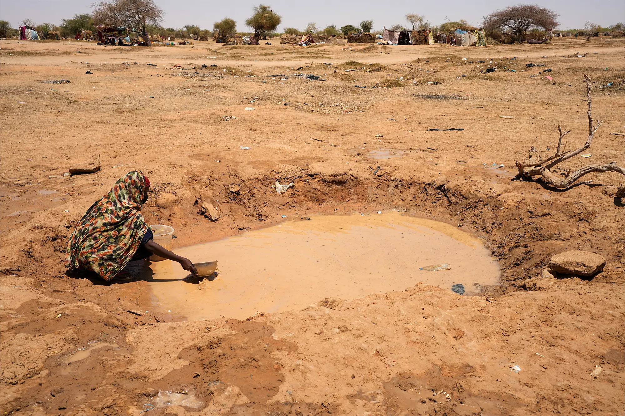 Una mujer recoge agua de un charco. El agua potable escasea considerablemente en el campamento de Oure Cassoni. Tras evaluar la situación, por el momento, suministramos agua mediante camiones cisterna mientras exploramos intervenciones más sostenibles.