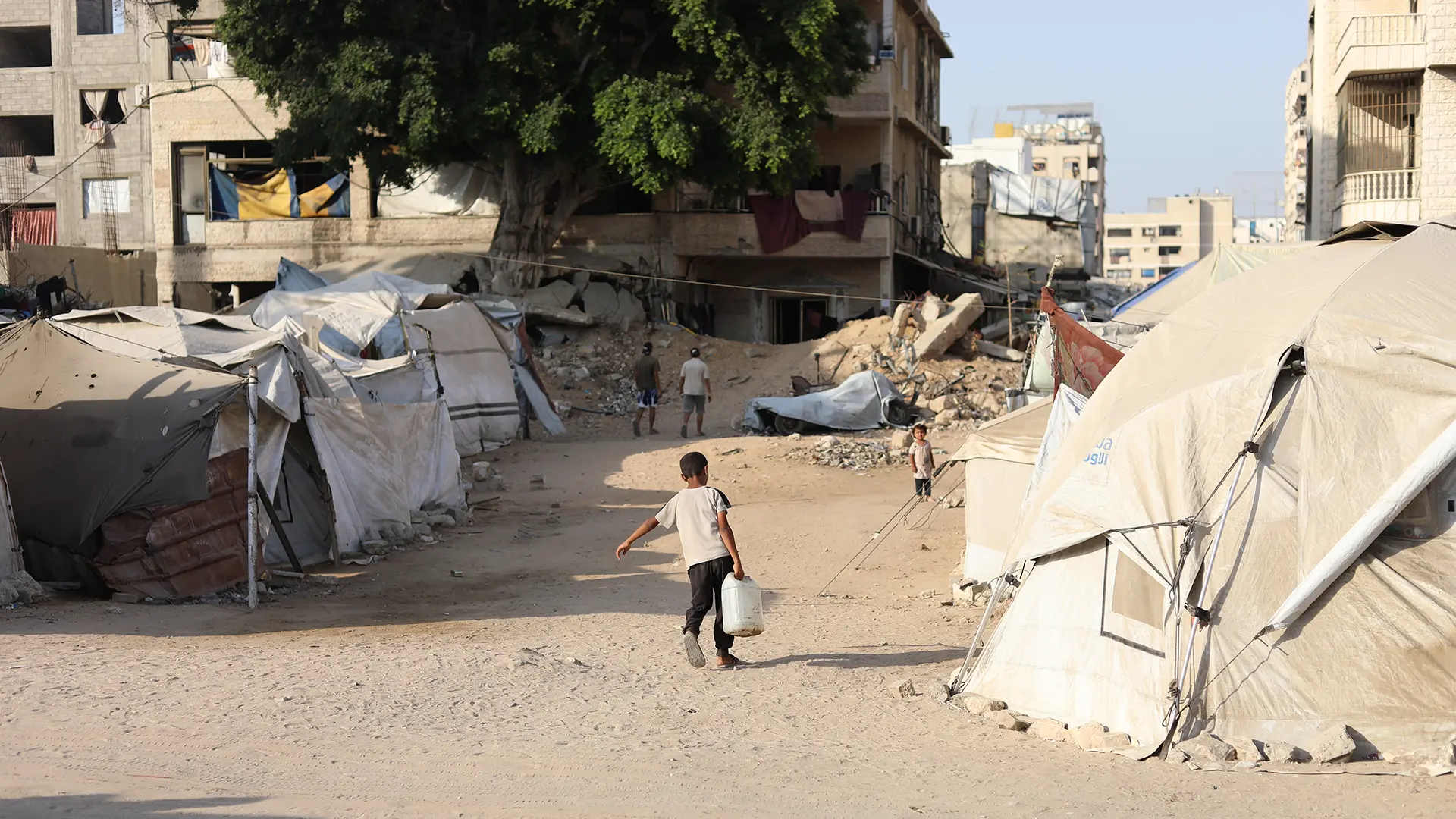 Un niño pequeño lucha bajo el peso de un bidón de agua para llevarlo a la tienda de campaña de su familia desplazada,mietras que Israel privan de agua a población de Gaza