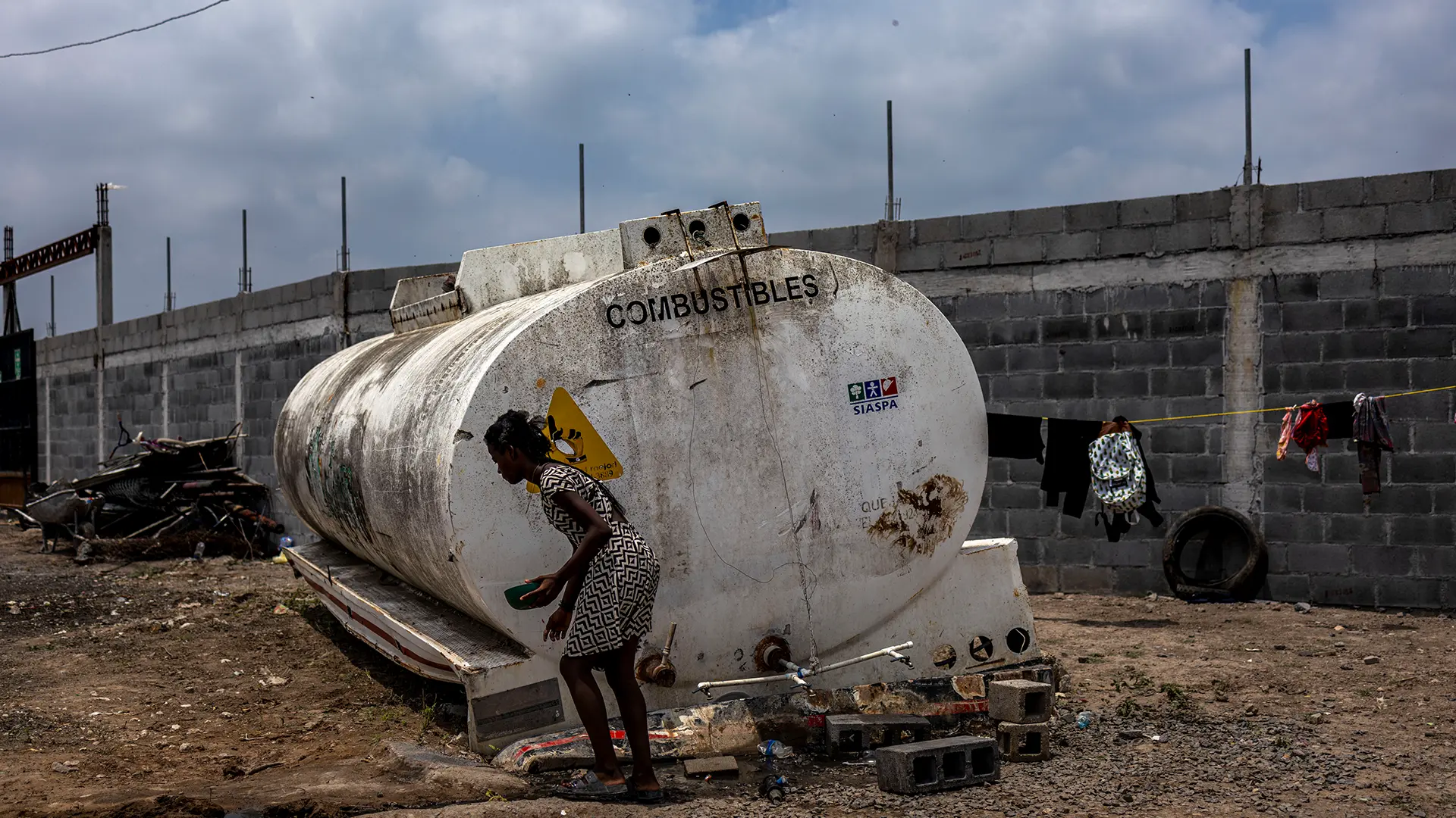 Una mujer haitiana recoge agua de un viejo tráiler de transporte de combustibles que está siendo usado como tanque de agua. No hay suficiente espacio en los albergues locales, por lo que muchas personas migrantes viven en condiciones precarias con acceso limitado a lo esencial.