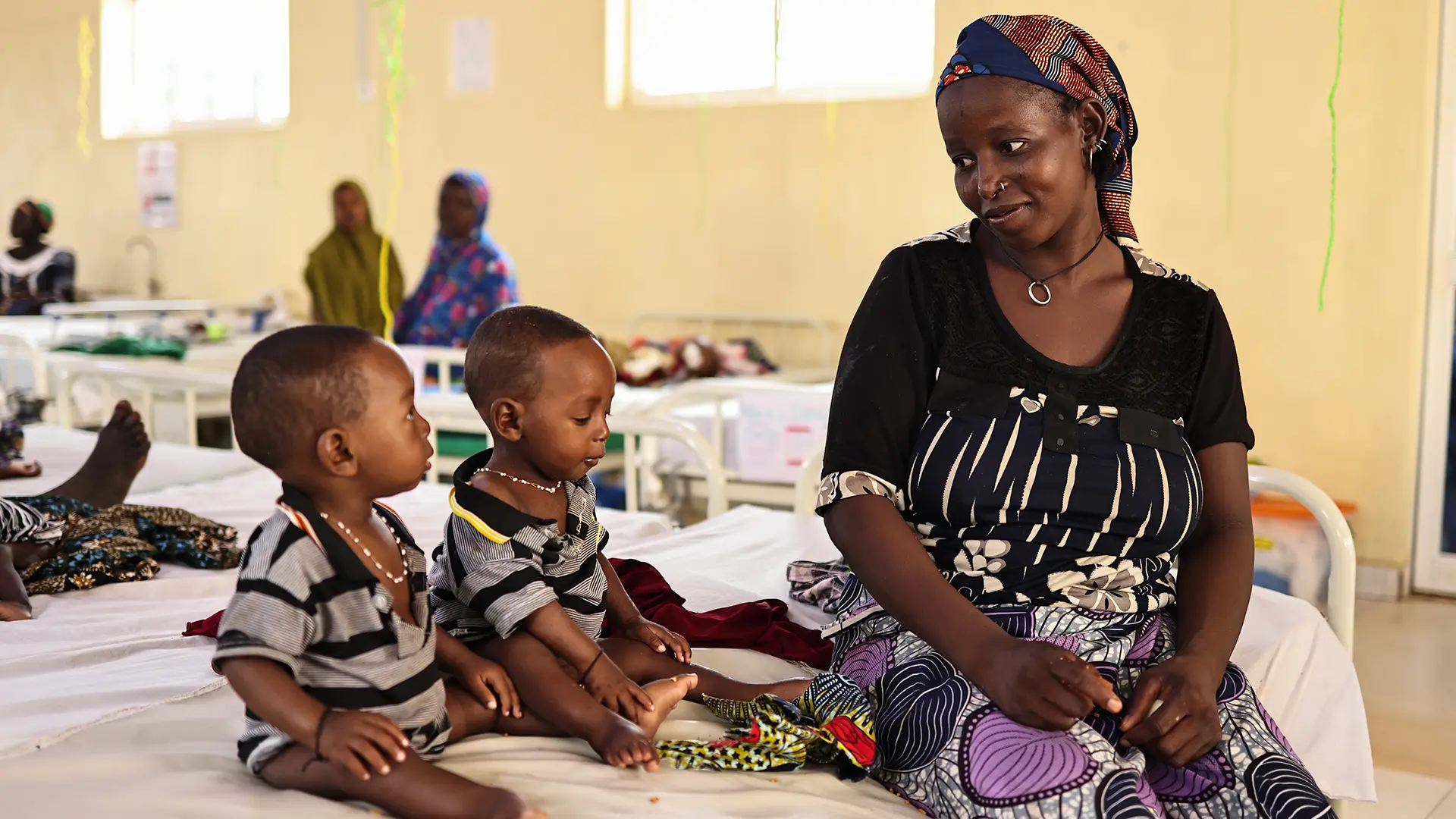 Binta Abdulraziqu junto a sus hijos gemelos, quienes fueron ingresados por desnutrición aguda grave en el centro de nutrición terapéutica para pacientes hospitalizados de Maiyama. Estado de Kebbi, Nigeria, agosto de 2025.