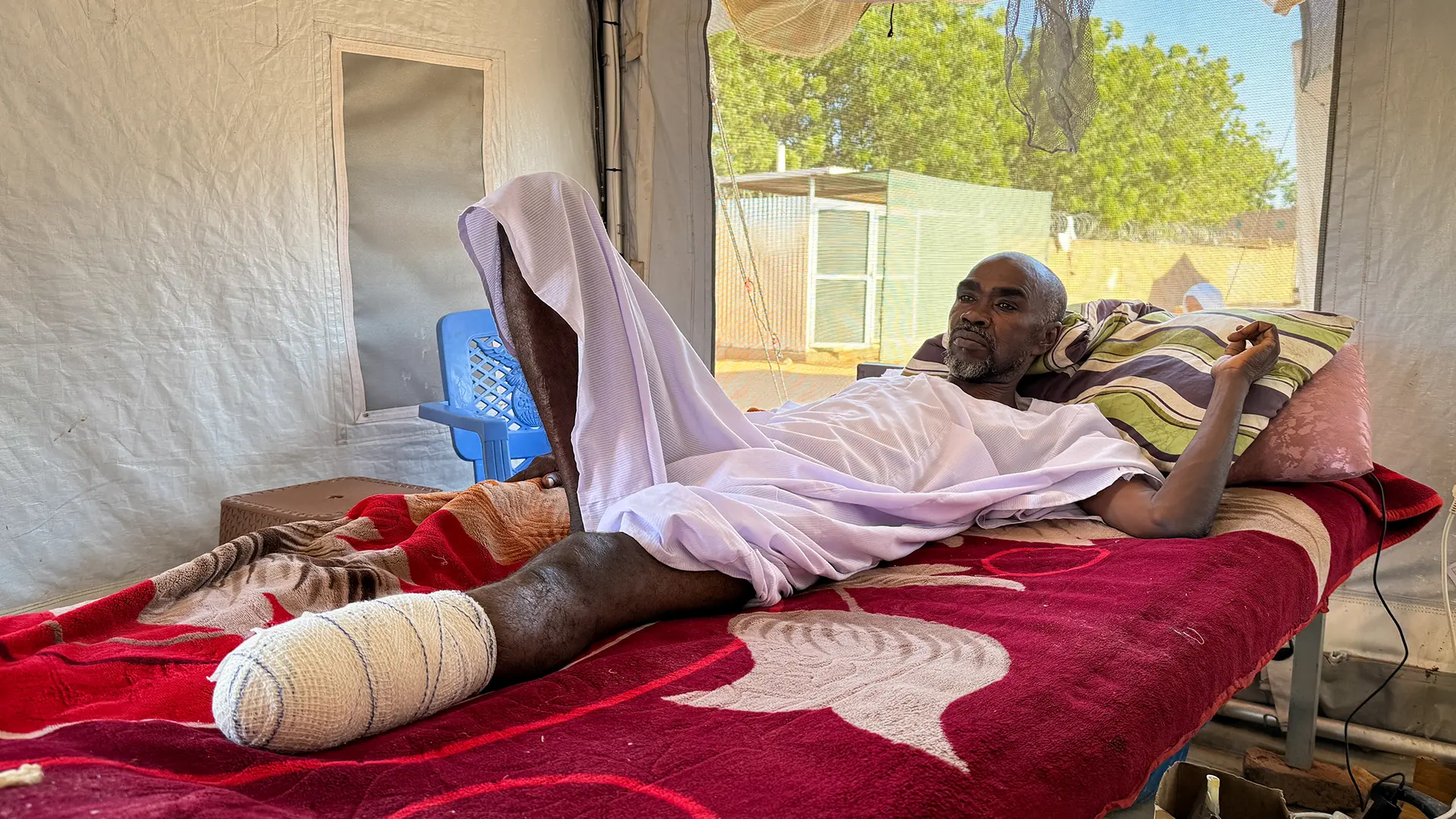 IA recibió un disparo en la pierna durante el tiroteo en El Fasher. Su hermano le hizo un torniquete con cartón y lo llevó en una carreta tirada por un burro hasta Tawila. Cuando llegó al hospital, los médicos tuvieron que amputarle parte de la pierna. Ahora espera recuperarse y encontrar un lugar seguro donde sus hijos puedan continuar su educación.