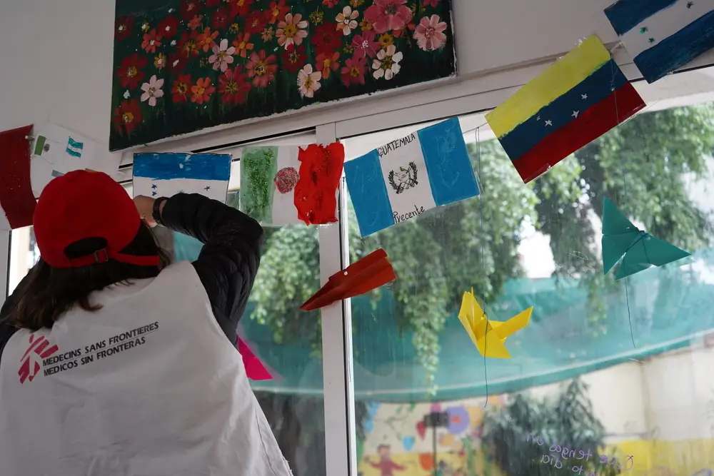 Una trabajadora de MSF decora una habitación con las banderas elaboradas por las personas atendidas en el Centro de Atención Integral (CAI) de MSF en la Ciudad de México.