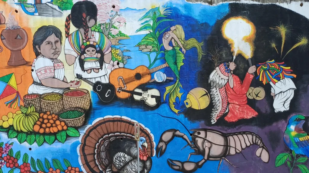 Este mural ubicado en la cabecera municipal de Huehuetla refleja la diversidad cultural del municipio y las diferentes cosmovisiones que coexisten, así como sus implicaciones al momento de la organización comunitaria.